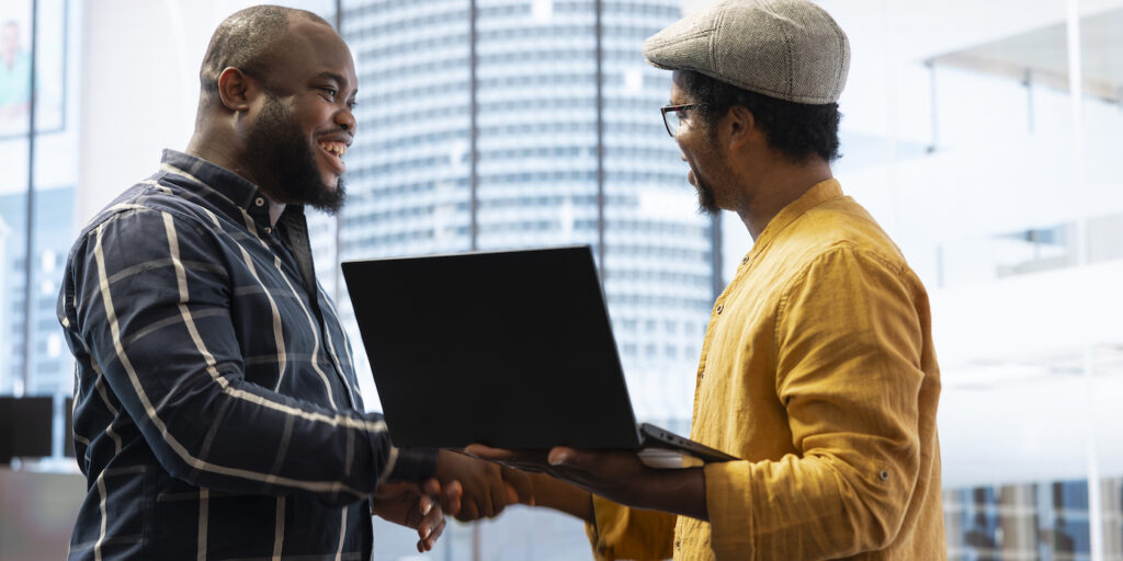 Two men shake hands while standing and smiling.