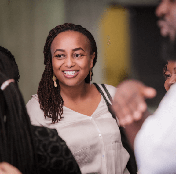 A woman with braids smiling warmly during a conversation with others